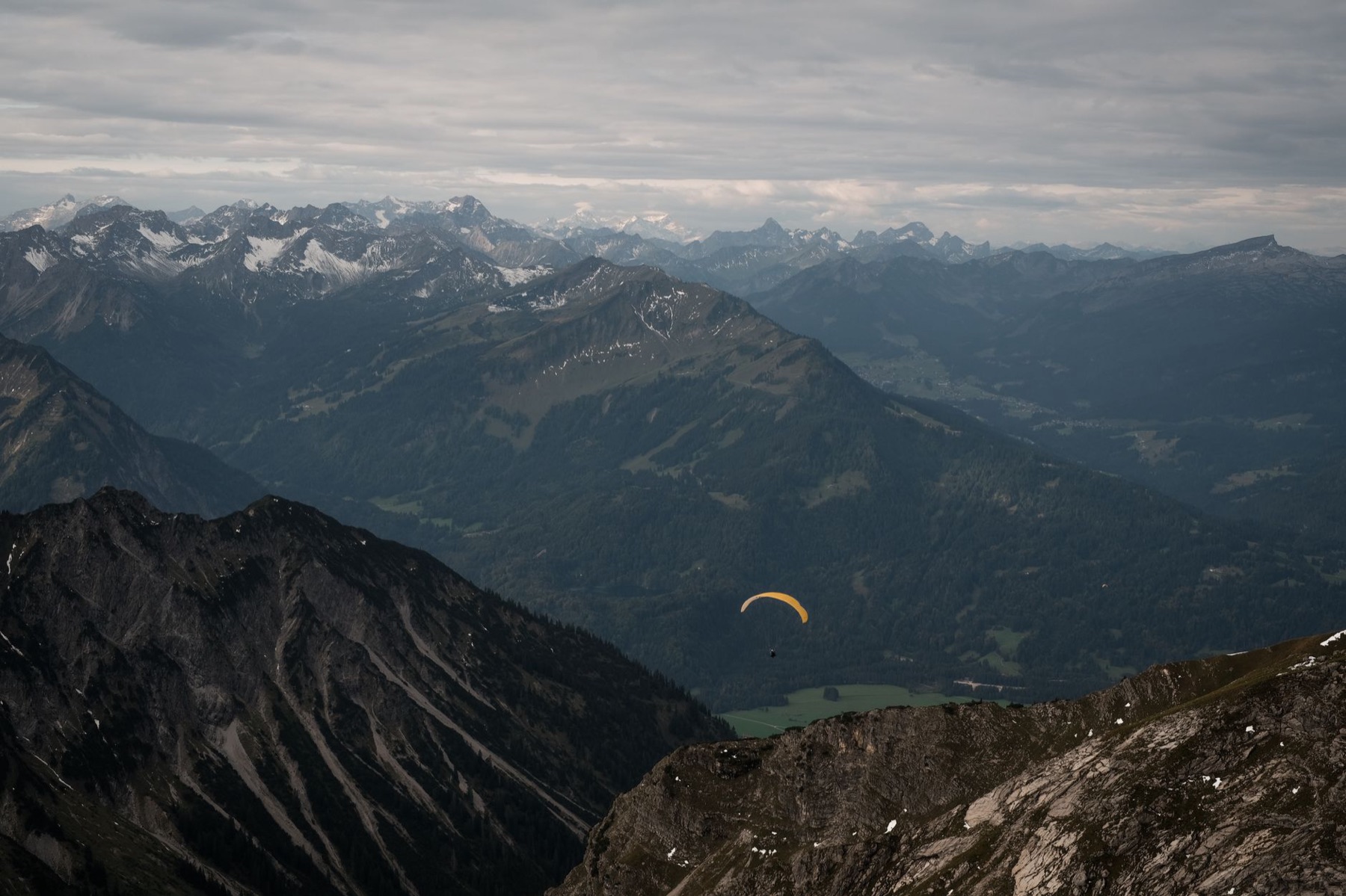 Parapente amarillo volando sobre un valle de montañas